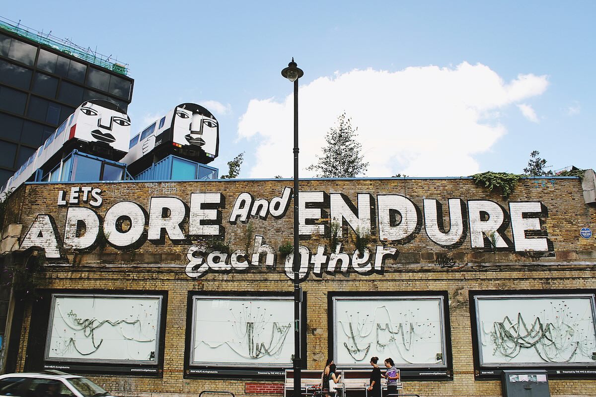Shoreditch street art mural in London reading “Let’s adore and endure each other” on a brick wall